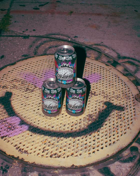 Three GAS cans stacked on a spray-painted smiley-face manhole cover.