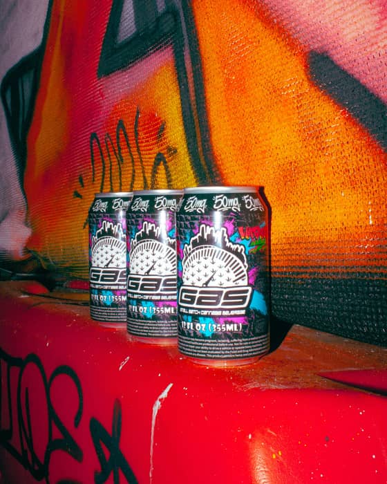 Three GAS cans on a red ledge in front of an orange and red graffiti mural.
