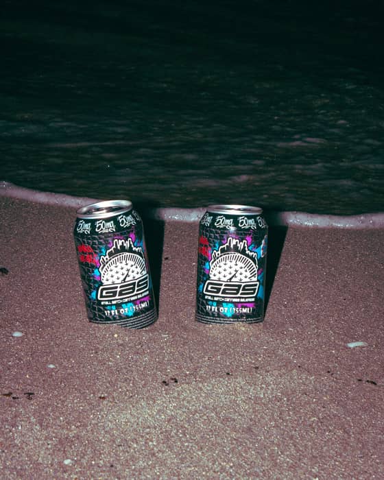 Two GAS cans standing in wet sand at the edge of the surf at night.